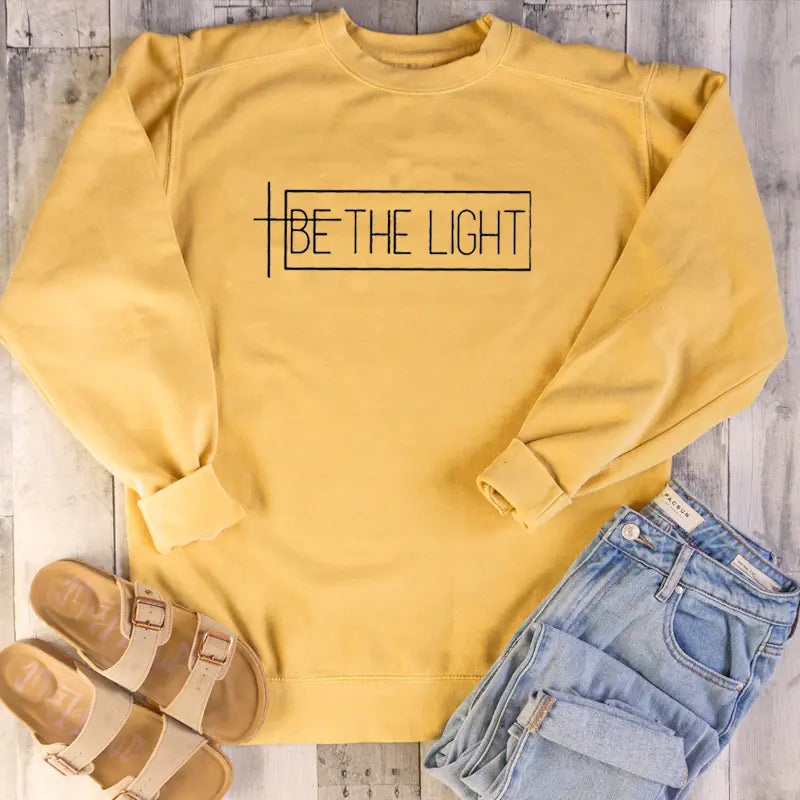 Yellow BE THE LIGHT sweatshirt styled with jeans and sandals, perfect for trendy streetwear.