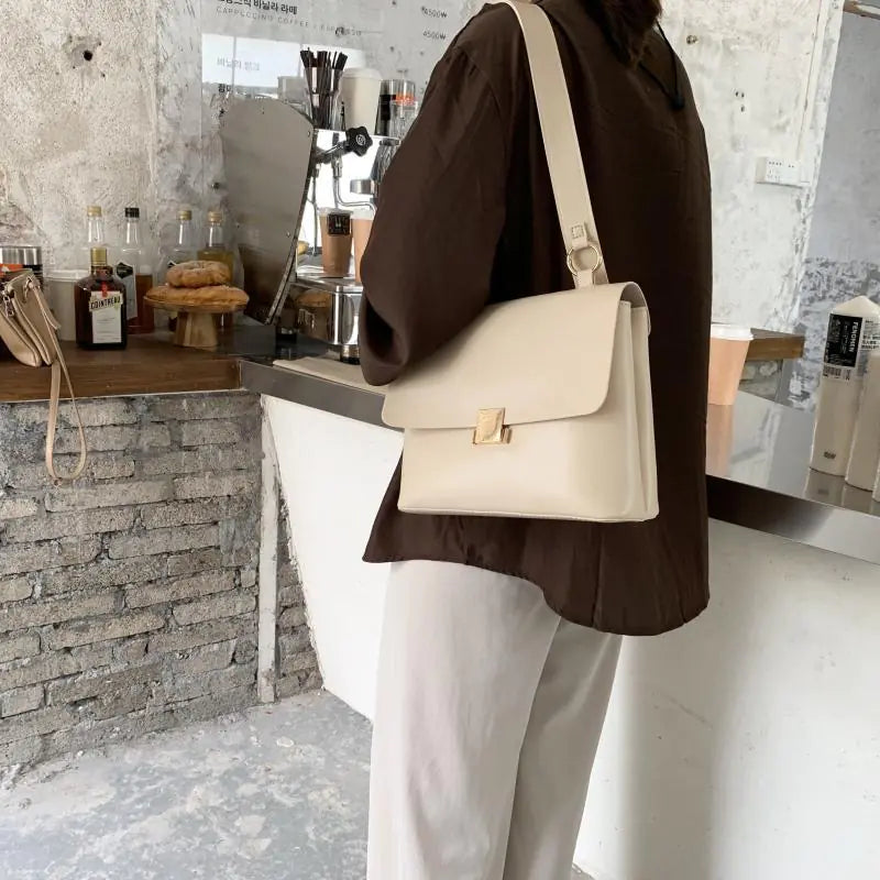 Woman wearing a vintage shoulder bag in a stylish café setting, showcasing its elegant design and large capacity.