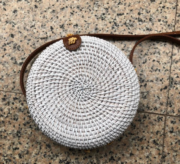 Woven rattan mini bag with leather closure, showcasing a round design and intricate straw weaving in a natural aesthetic.