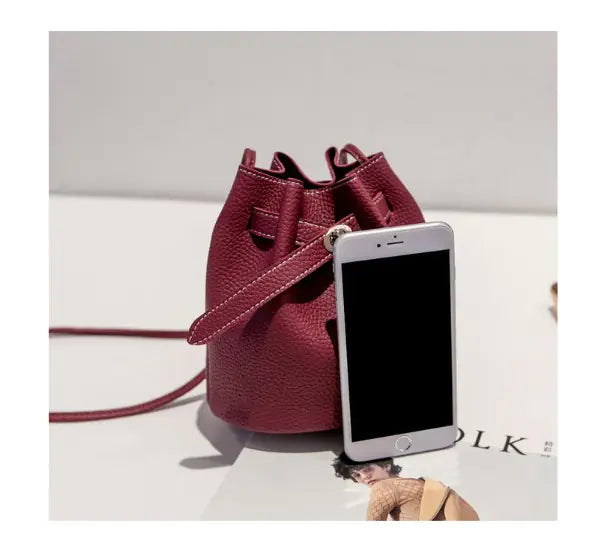 Stylish burgundy bucket bag with smartphone, showcasing versatile design and luxury aesthetic.