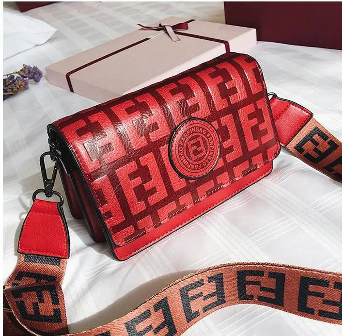 Red mini shoulder bag with logo and patterned strap, perfect for a chic retro style.