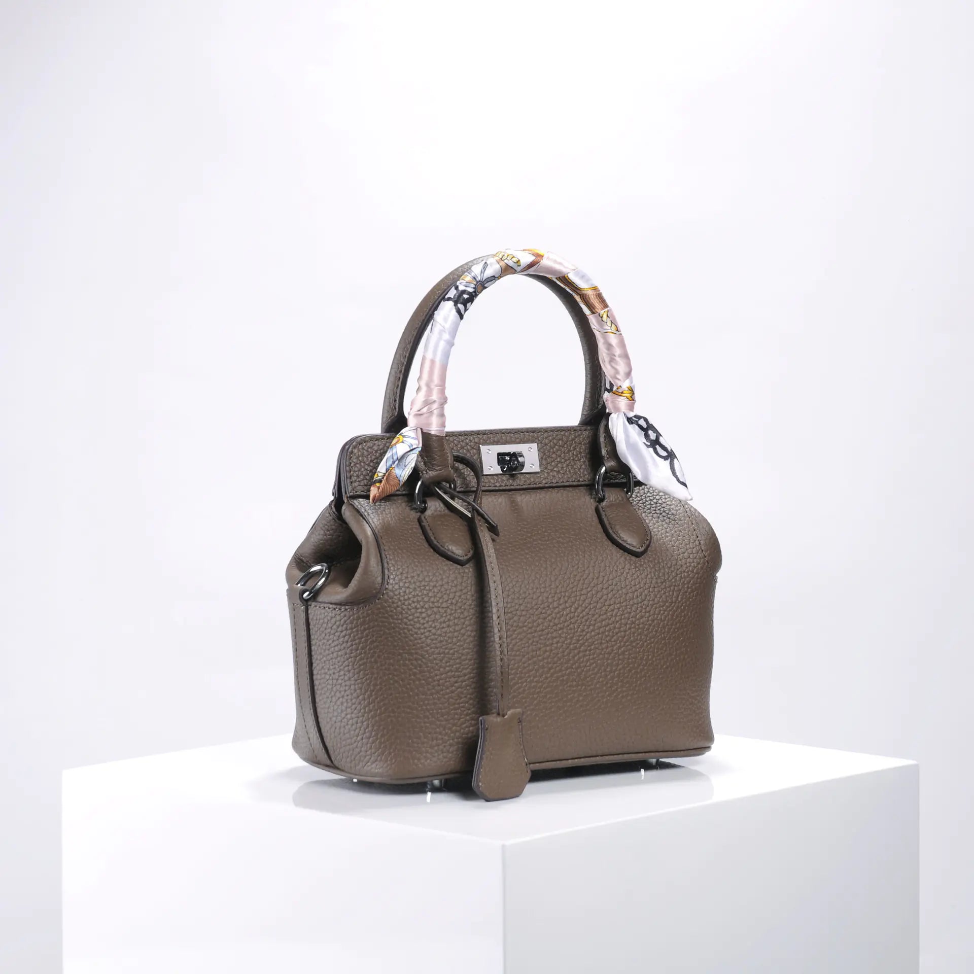 Chic brown handbag with a patterned scarf handle on a display pedestal, showcasing luxury and style.