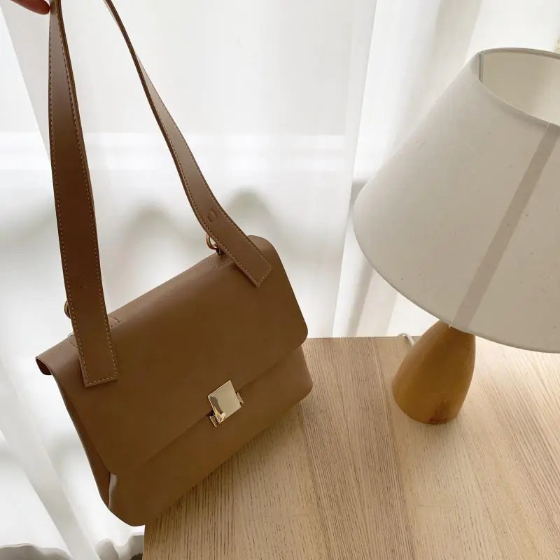 Vintage shoulder bag for women, large capacity crossbody in brown, displayed beside a lamp on a wooden table.