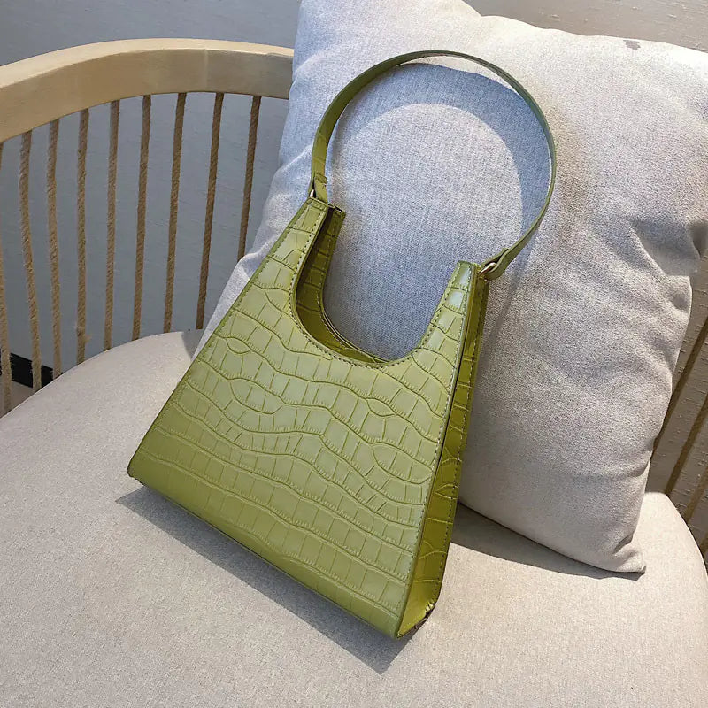 Vintage women's handbag with crocodile texture in green on a soft cushion.