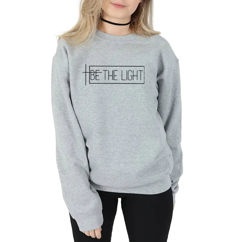 Woman wearing BE THE LIGHT streetwear sweatshirt in gray, highlighting stylish expression and comfort.