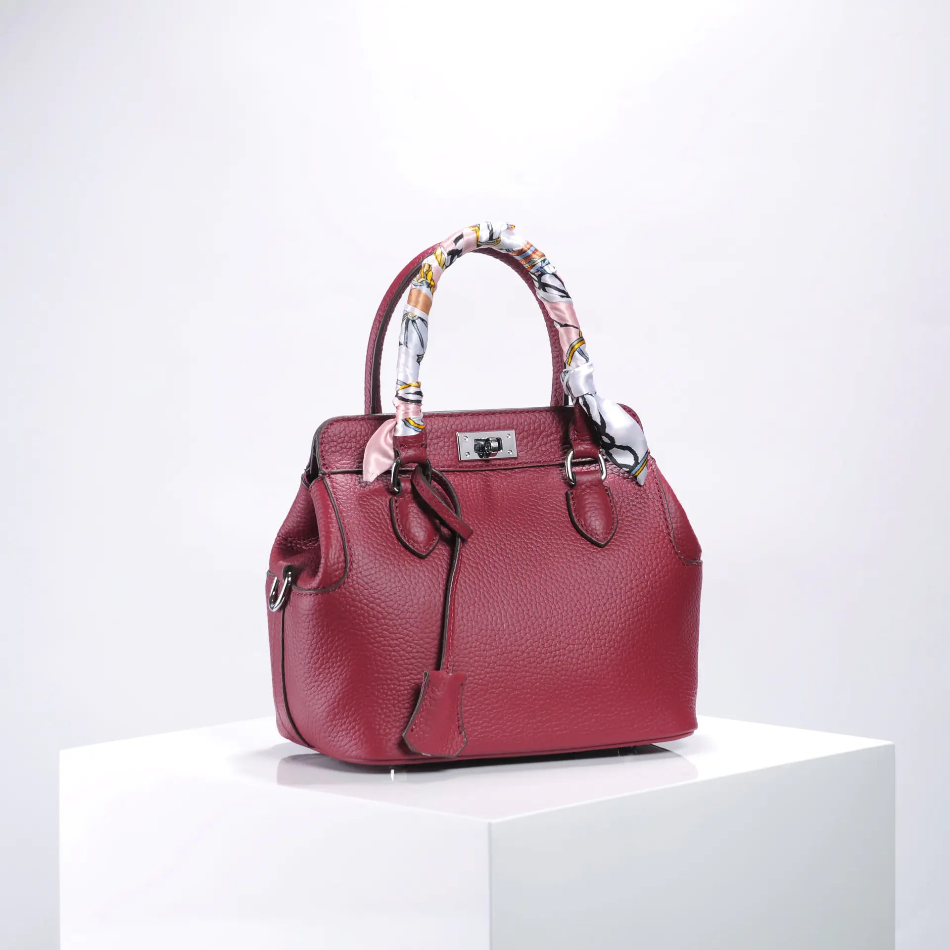 Elegant red handbag with patterned scarf handle, showcasing luxury leather craftsmanship.