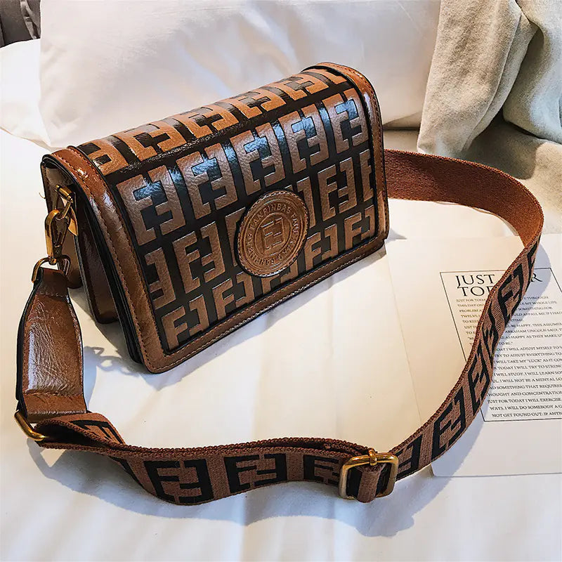 Vintage shoulder crossbody bag with stylish embossed pattern and adjustable strap on a soft surface.