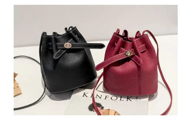 Stylish black and burgundy bucket bags with drawstring closures displayed on a table.