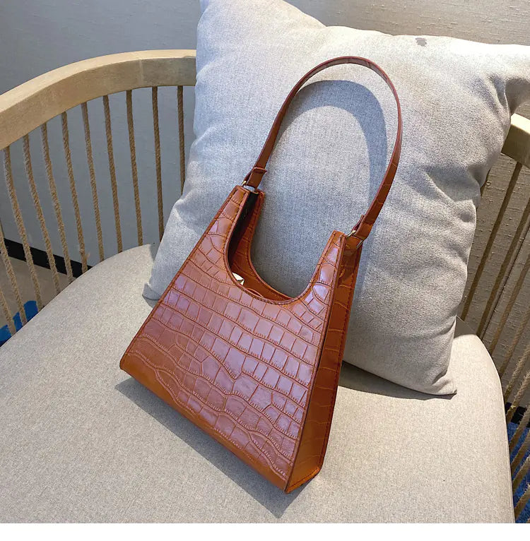 Vintage women's crocodile texture handbag in brown, showcasing chic design on a cozy chair.
