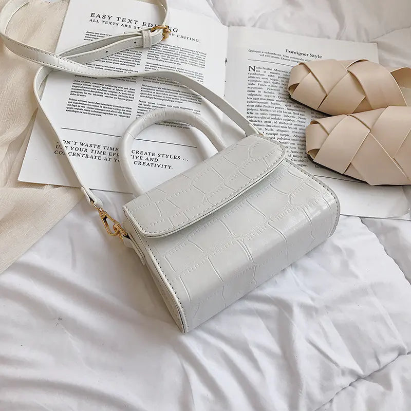 Mini stone pattern handbag in white, stylish crossbody bag on a bed with magazines and shoes.