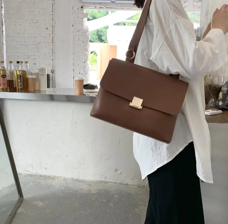 Vintage brown shoulder bag with gold clasp, stylish and functional for women, shown in a modern cafe setting.