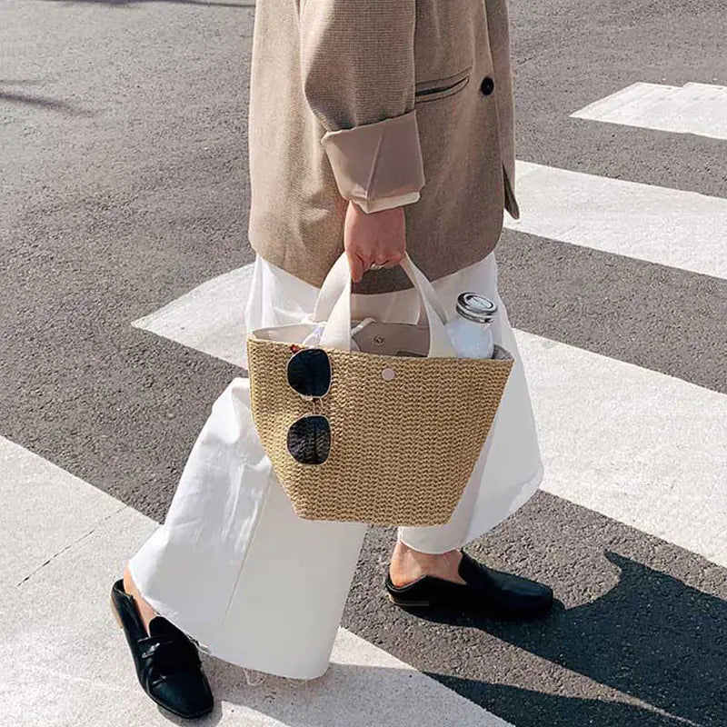 Woven grass straw tote bag in bucket style, perfect for beach outings, featuring stylish sunglasses and a modern design.