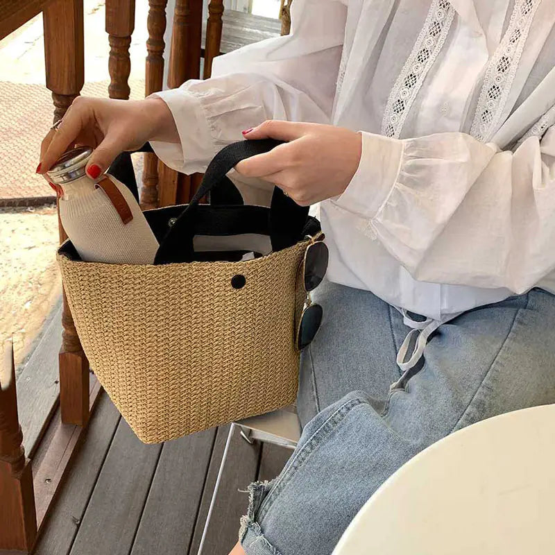 Woven straw tote bag in beach bucket style held by a person, showcasing minimalistic design and functionality.