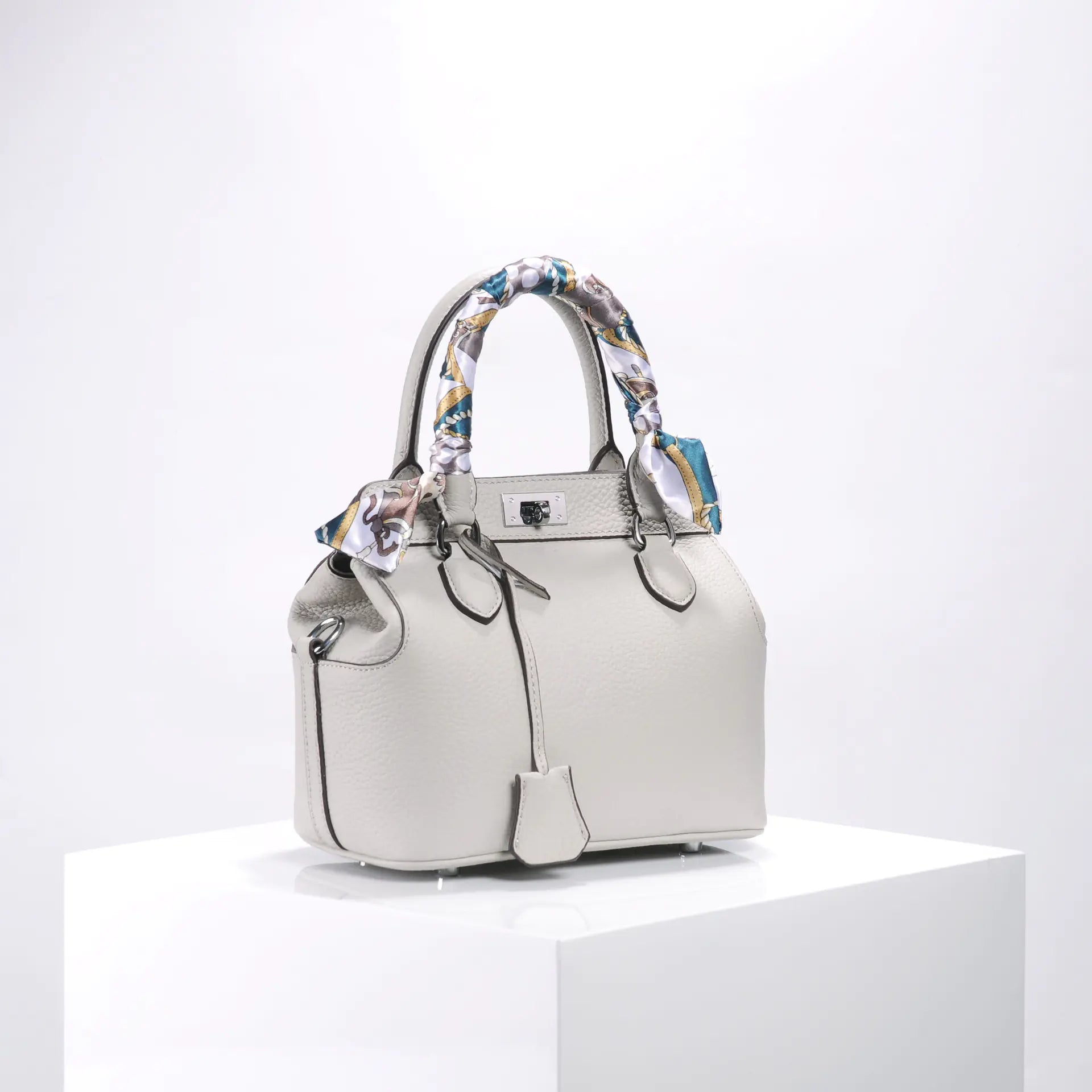 Stylish beige handbag with patterned scarf handle, showcasing luxury and elegance.