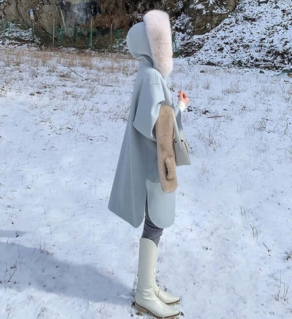 Woman in a gray oversized coat with a fur hood standing in snow, showcasing winter fashion style.