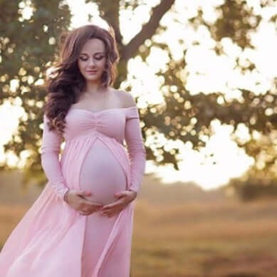 Pregnant woman cloak dress in pink chiffon, long sleeve, showcasing baby bump outdoors.