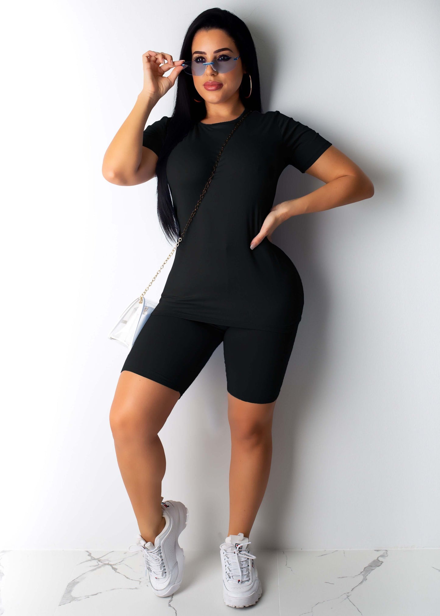Casual woman solid color sportswear in black with sunglasses and stylish sneakers.