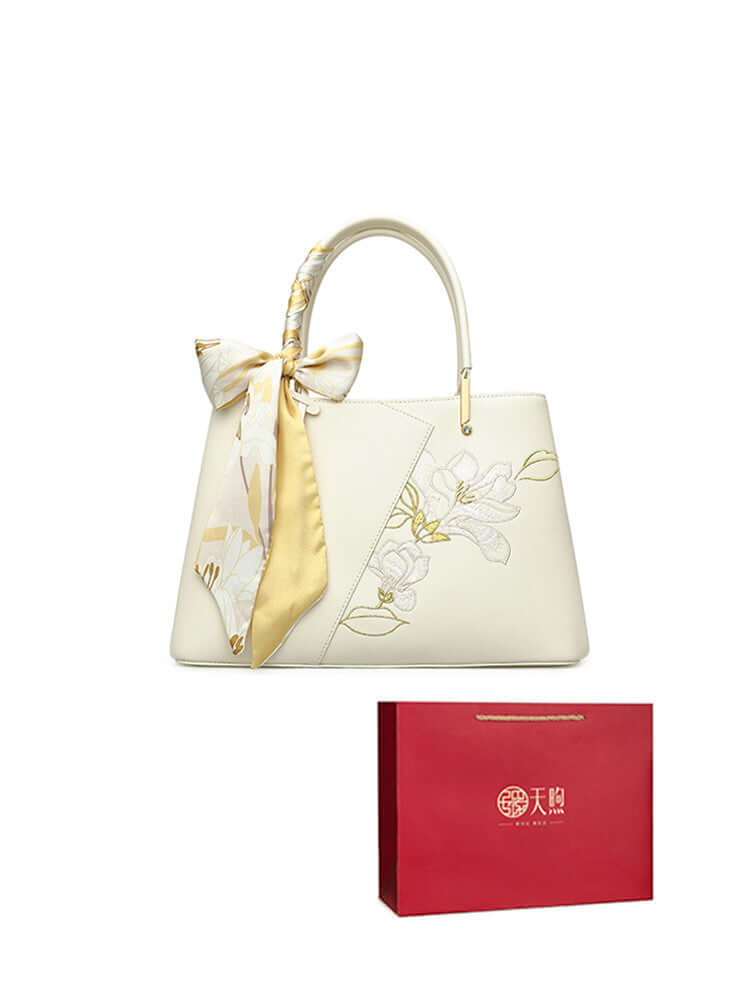 Pearl cowhide handbag with floral design and ribbon, paired with elegant gift packaging.